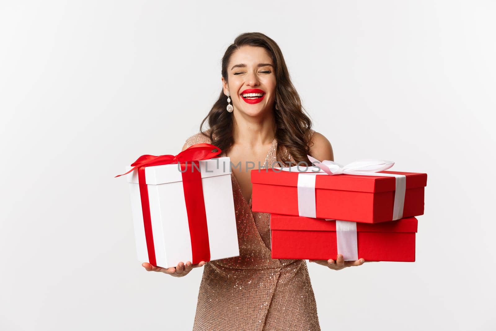 Holidays, celebration concept. Beautiful caucasian woman in elegant dress holding Christmas presents and smiling happy, standing over white background.