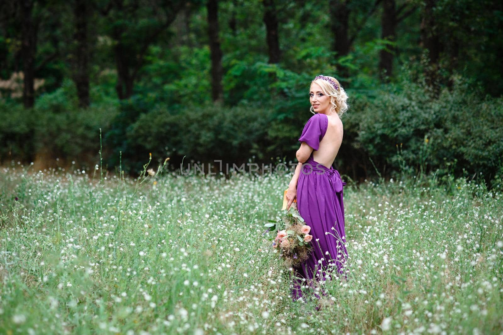 Girl model blonde in a lilac dress with a bouquet with a green forest