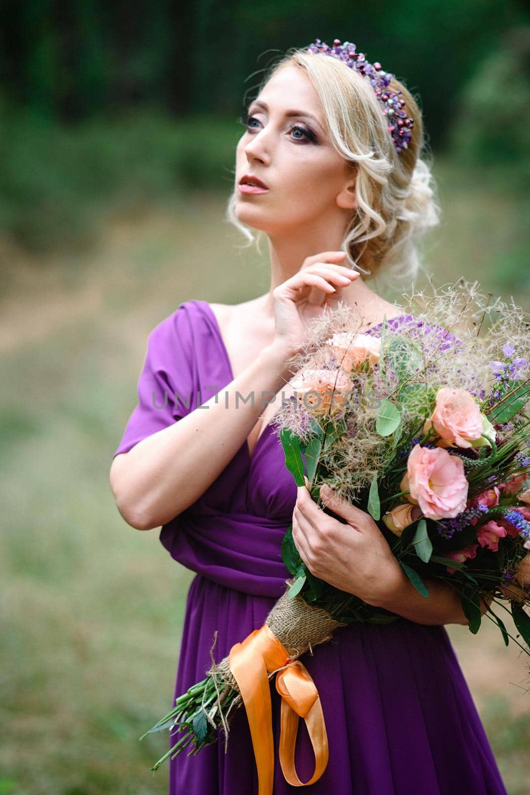 Girl model blonde in a lilac dress with a bouquet with a green forest