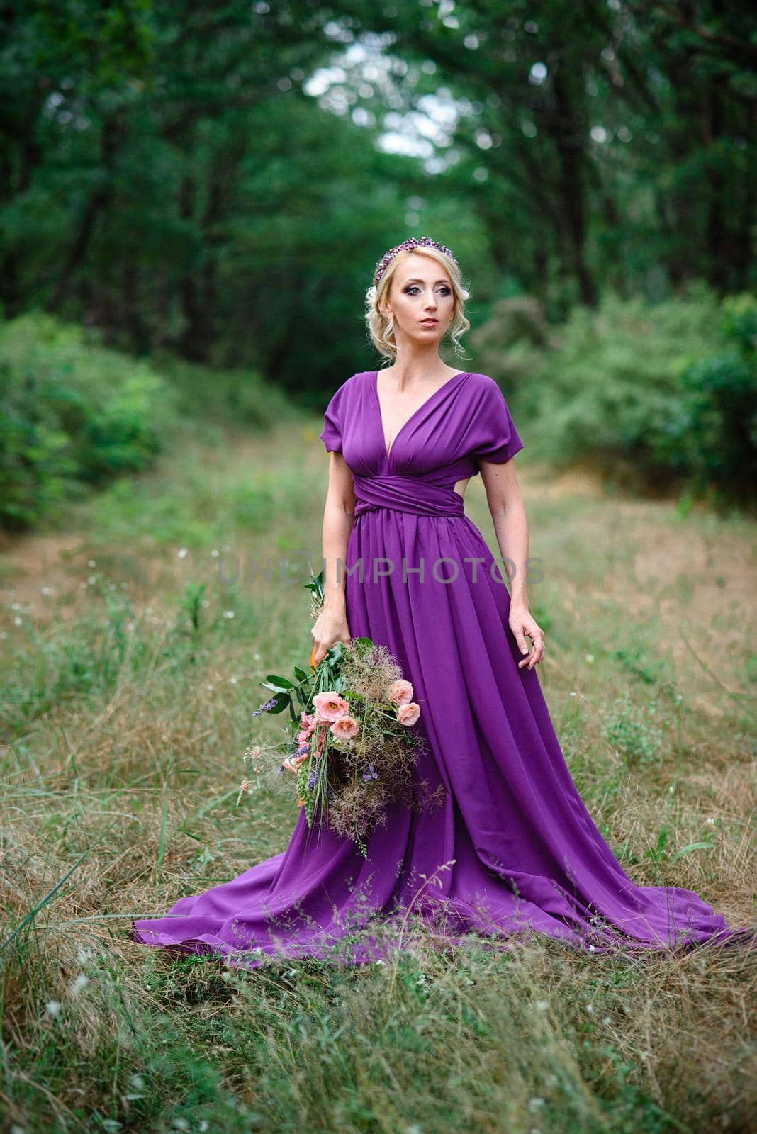 Girl model blonde in a lilac dress with a bouquet with a green forest