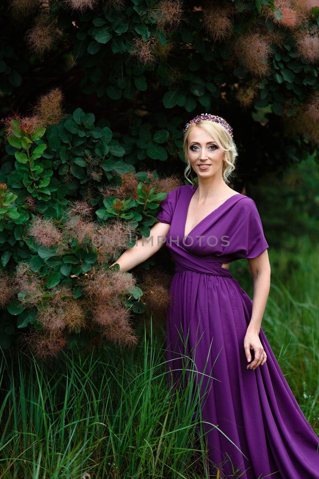 Girl model blonde in a lilac dress with a bouquet with a green forest