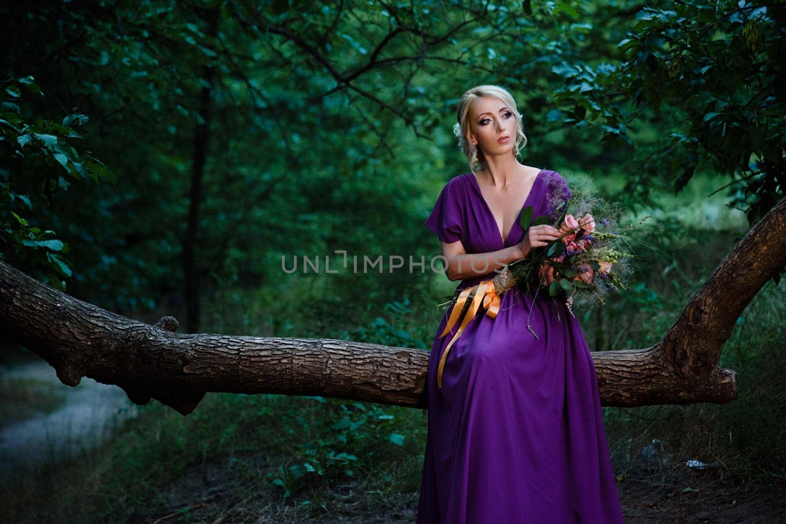 Girl model blonde in a lilac dress with a bouquet with a green forest