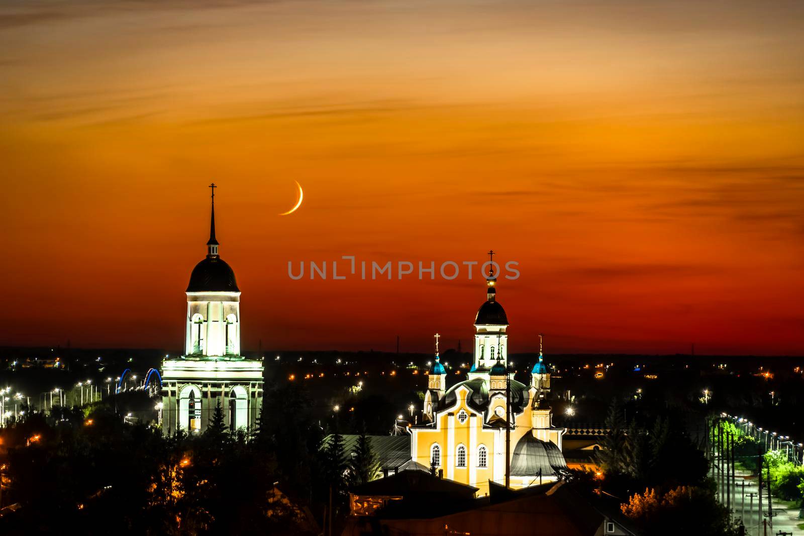 A church,temple or cathedral against the background of an evening sunset with a maroon sky and a big month.The horizon line at dawn with the moon and the red sky.City panorama with towers and domes by YevgeniySam