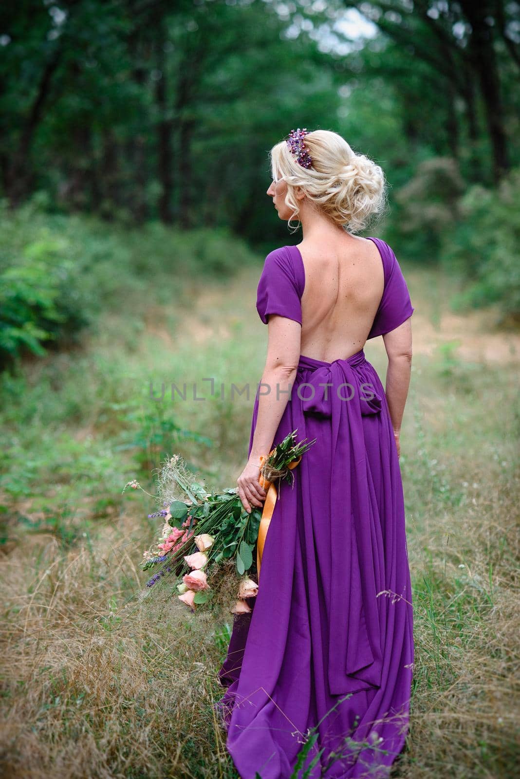 Girl model blonde in a lilac dress with a bouquet with a green forest