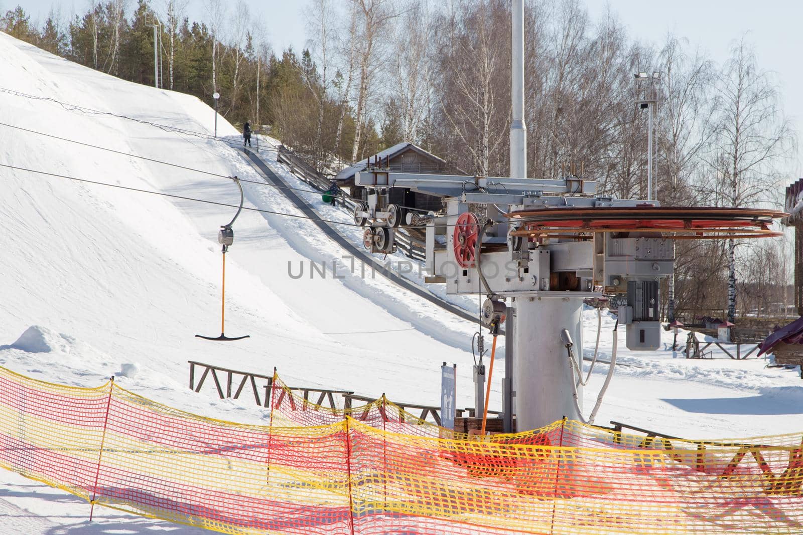 Rotating cable car lift in a ski resort. Lighting pillars and trees against the blue sky. Mountain slope equipment for snowboarding. Ski tours on a sunny day.