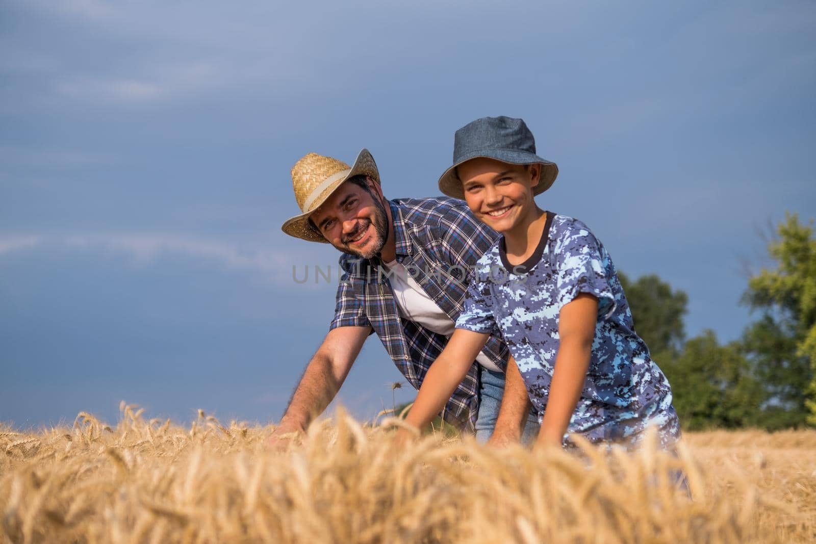 Happy father and son are standing in their grown wheat field before harvest.