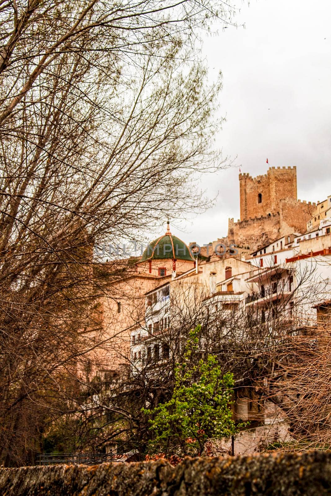 Beautiful overview of the town of Alcala de Jucar with the fortress castle and the church in spring under gray sky