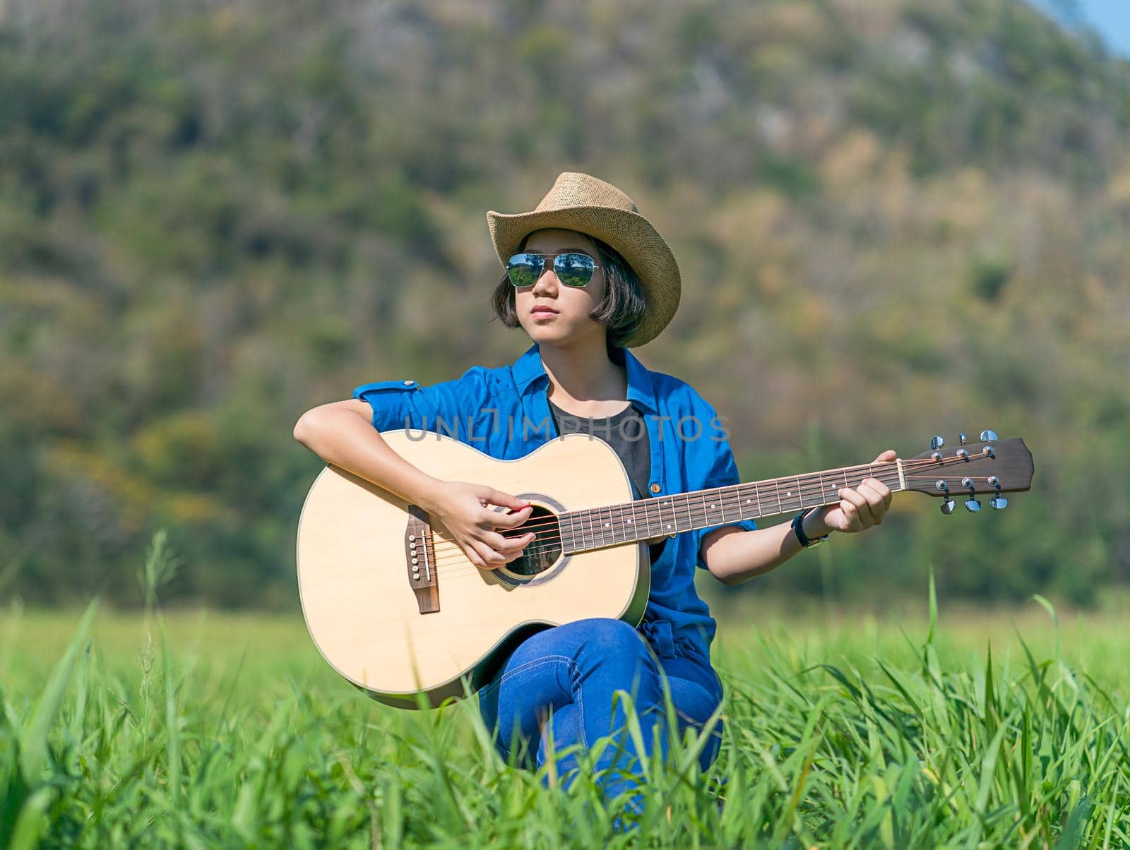 Women short hair wear hat and sunglasses sit playing guitar in grass field  by stoonn