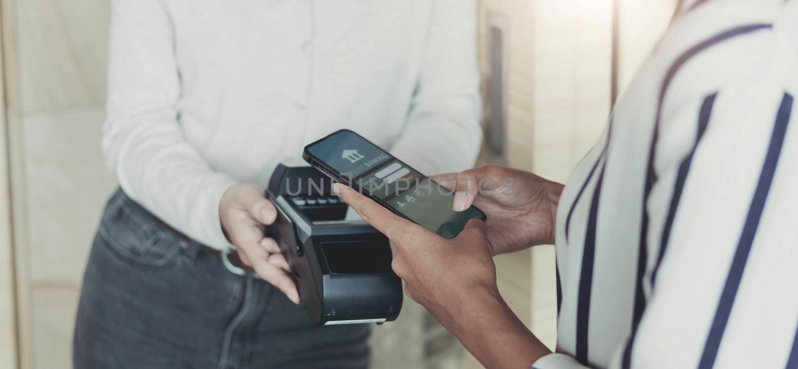 Woman paying bill through smartphone using NFC technology in a coffee. customer paying through mobile phone using contactless technology. Closeup hands of mobile payment at a coffee shop