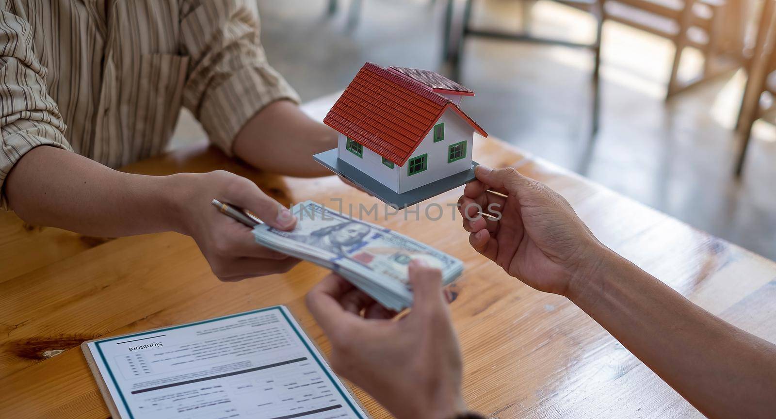 business people handing over dollars with decorative house model and contract at office.