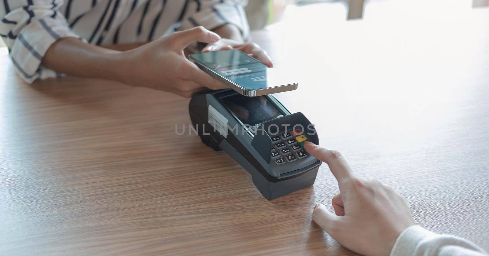 Woman paying bill through smartphone using NFC technology in a coffee. customer paying through mobile phone using contactless technology. Closeup hands of mobile payment at a coffee shop by wichayada