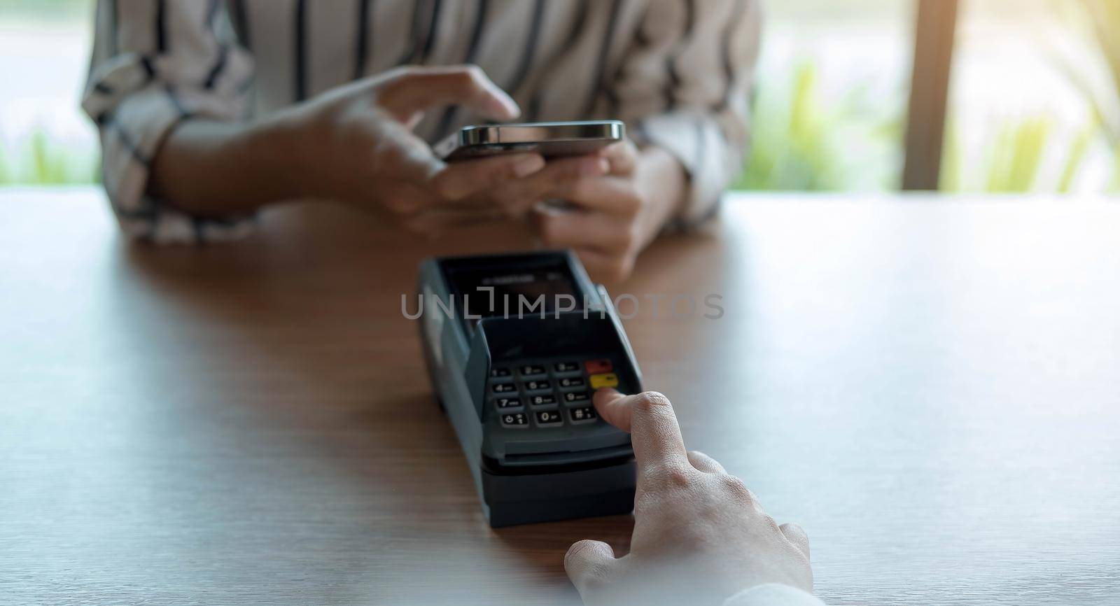 Woman paying bill through smartphone using NFC technology in a coffee. customer paying through mobile phone using contactless technology. Closeup hands of mobile payment at a coffee shop