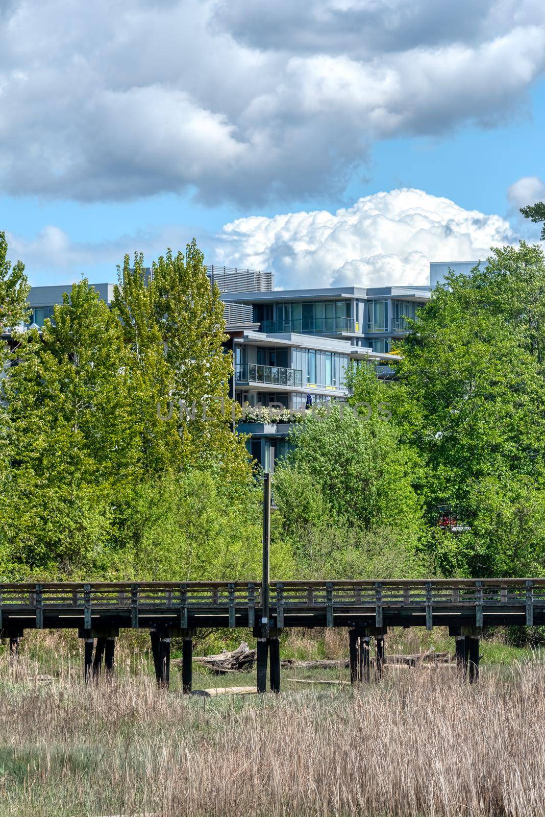 Eco cityscape. Wooden pier in front of residential building on cloudy sky background.