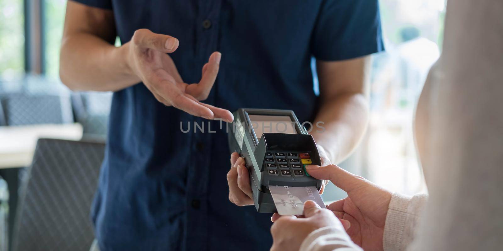 Hand of customer paying with contactless credit card with NFC technology. Bartender with a credit card reader machine at bar counter with female holding credit card. Focus on hands. by wichayada