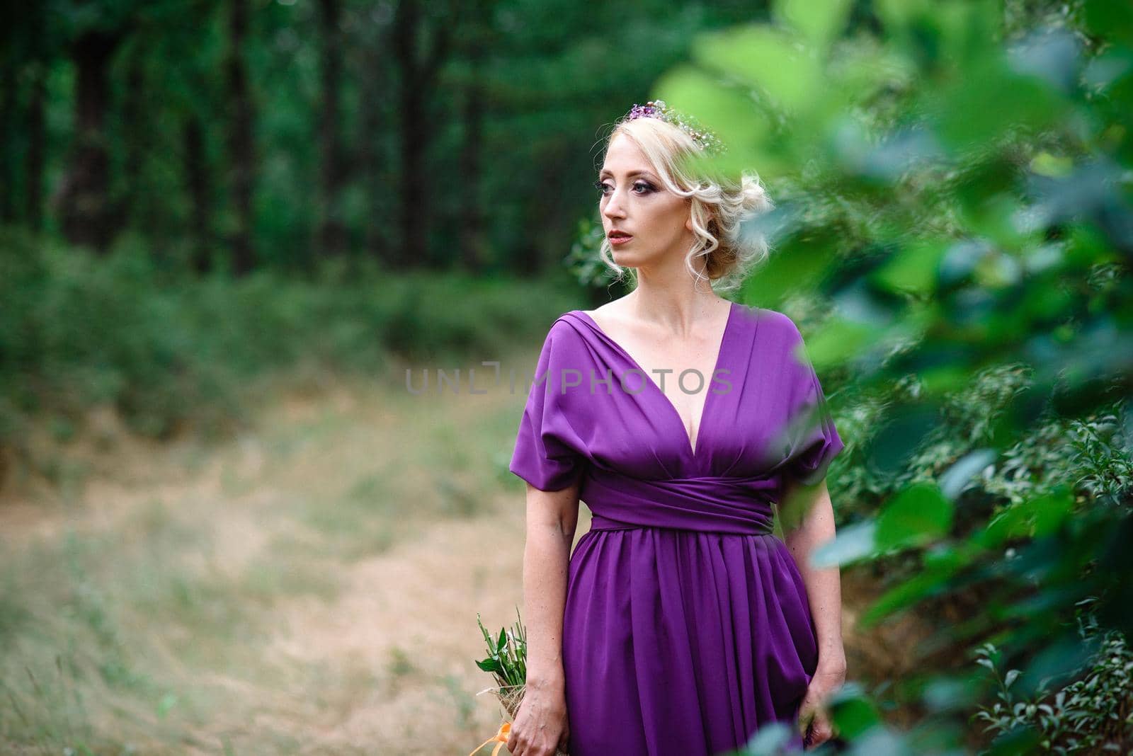 Girl model blonde in a lilac dress with a bouquet with a green forest