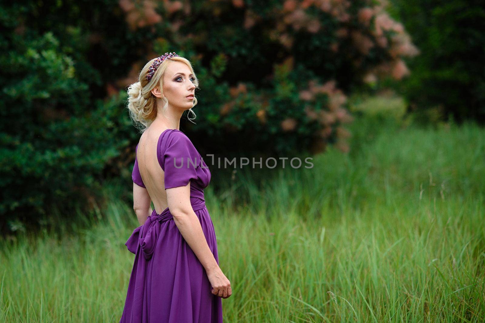 Girl model blonde in a lilac dress with a bouquet with a green forest