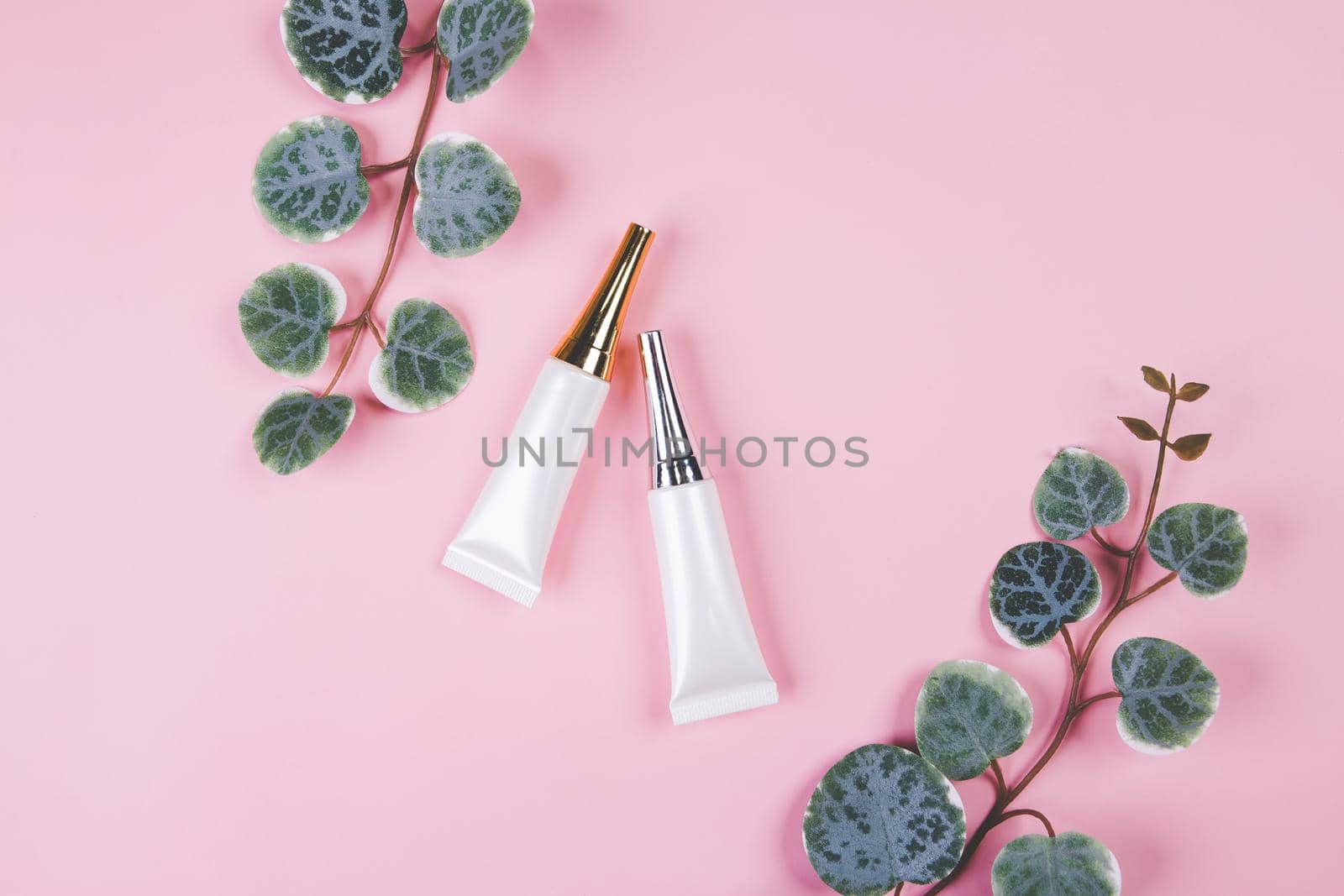 Mockup cosmetic tube with cream or lotion and leaf isolated on pink background, mock up package for advertising, skincare or cosmetology, top view, flat lay, skin care and treatment with product.