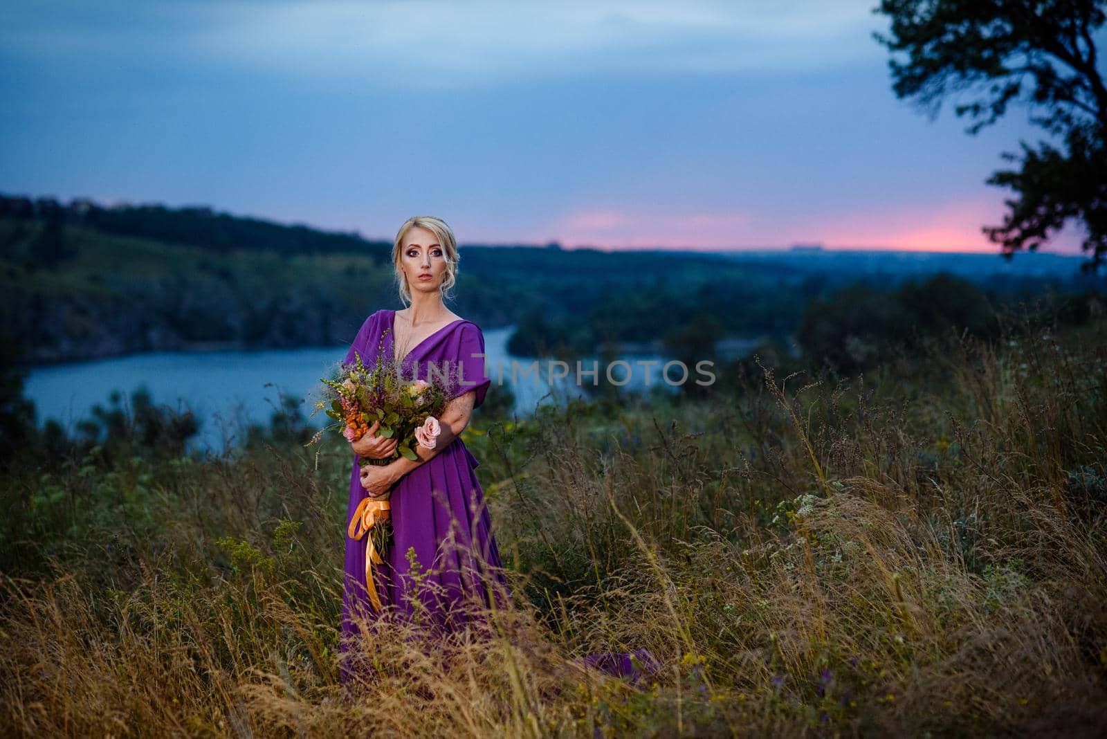 Girl model blonde in a lilac dress with a bouquet with a green forest