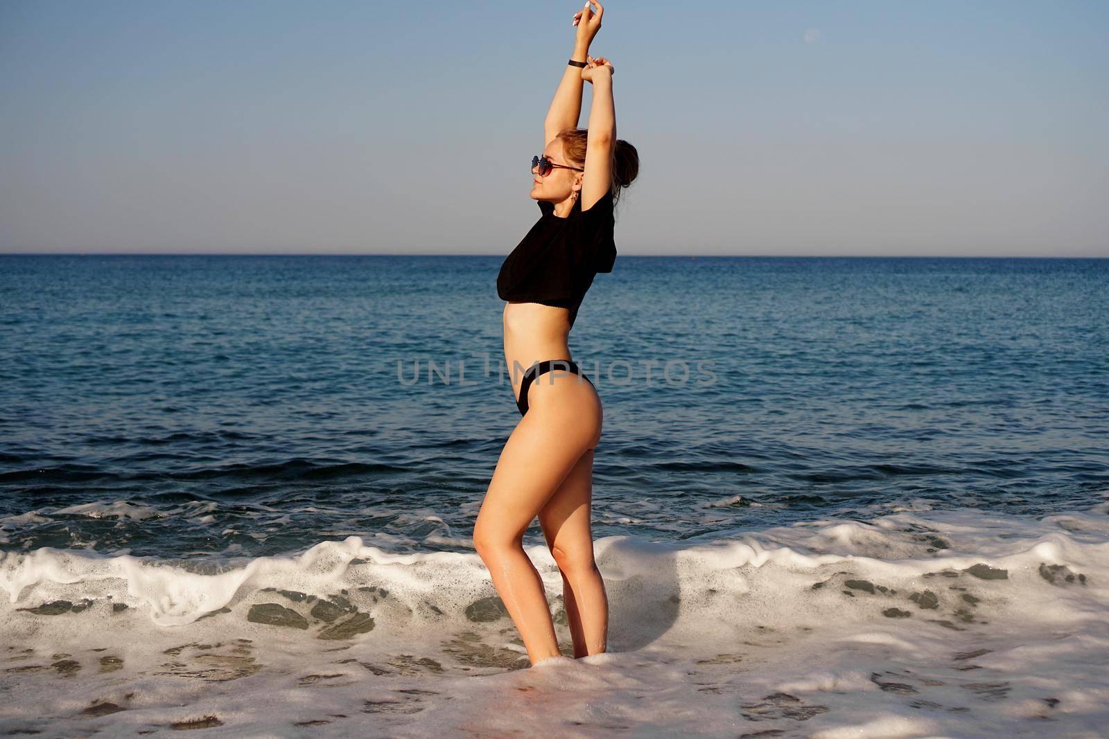 Young woman in a black tank top and underpants on the sea beach. Tanned body, body positive