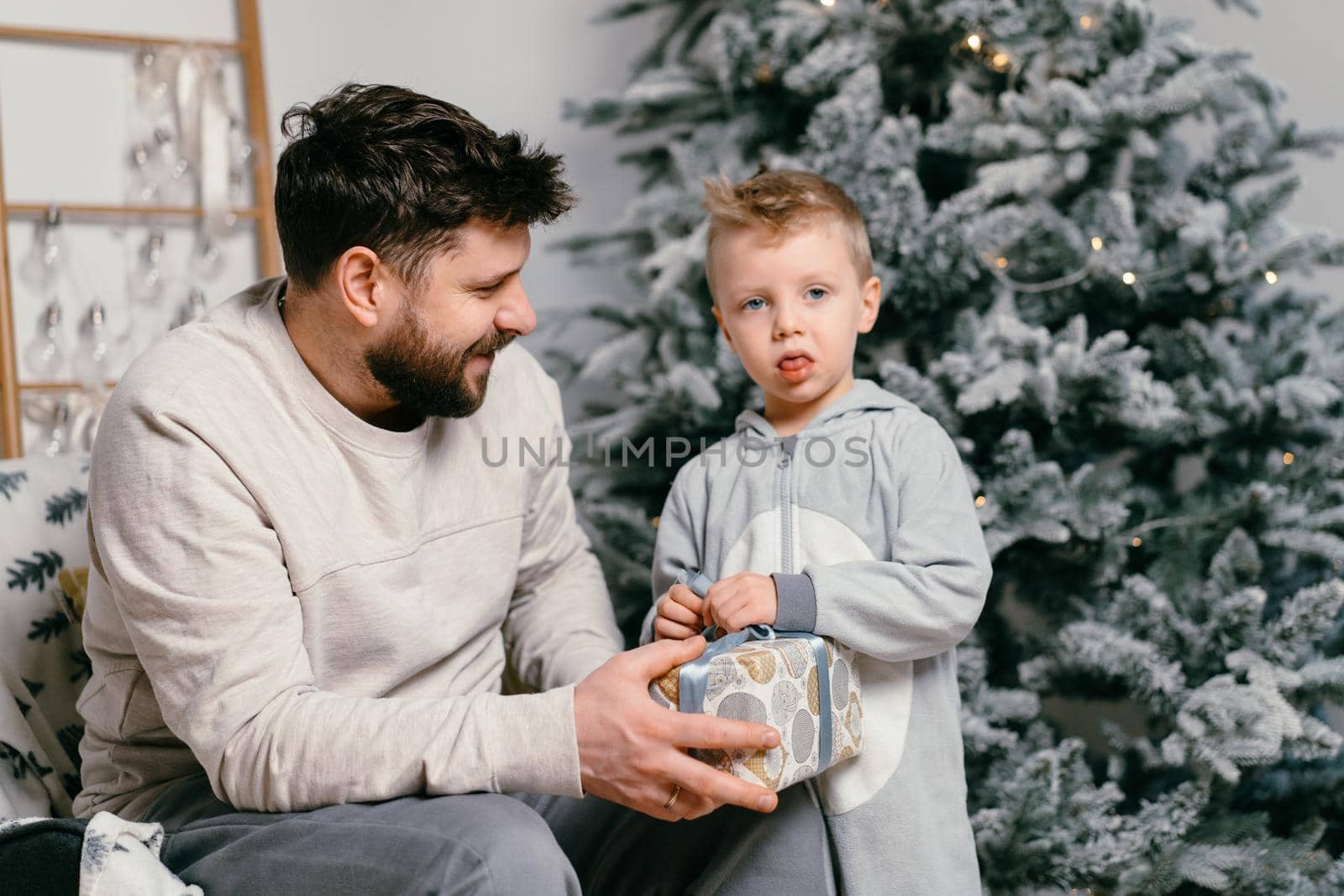 Holiday Christmas Handsome father playing with small cute son near decorated New year tree at home Family tradition father gives a gift to his little boy