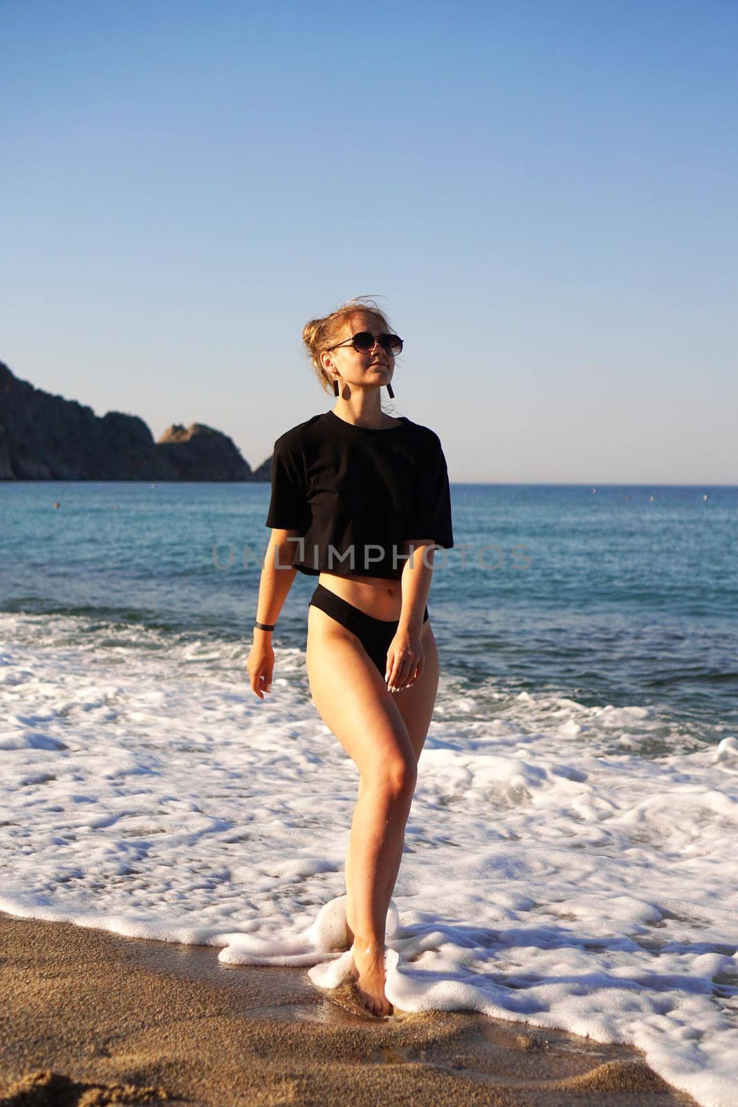 Young woman in a black tank top and underpants on the sea beach. Tanned body, body positive. Vertical photo