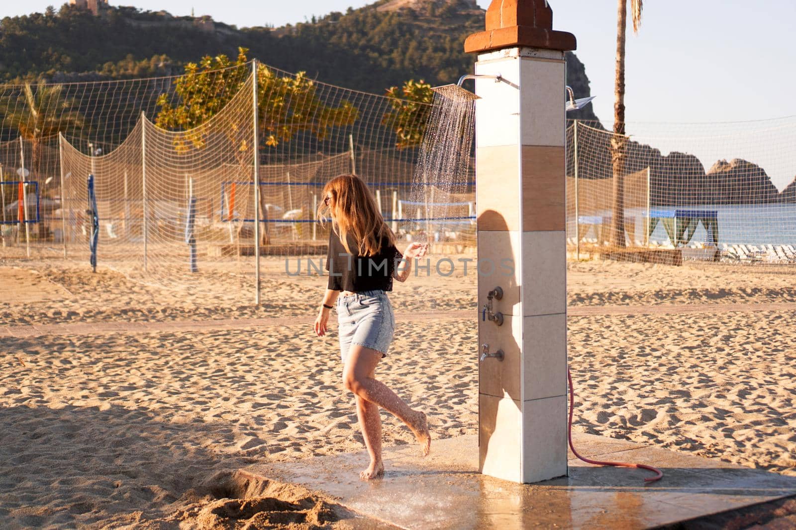 A girl in shorts and a black T-shirt on the beach near the shower. by natali_brill