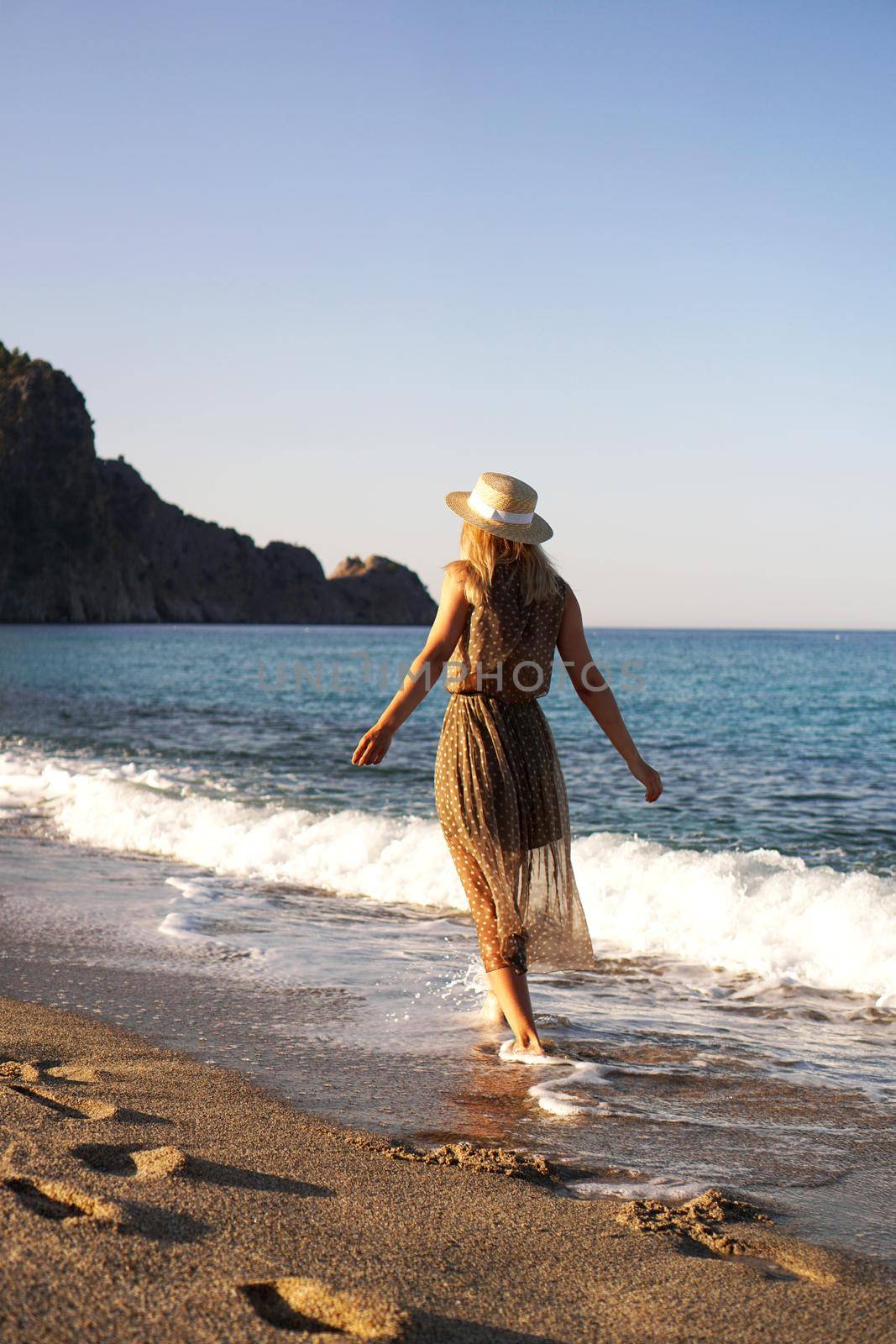 Woman on the beach in a brown dress and with a straw hat. Vacation on the beach by natali_brill