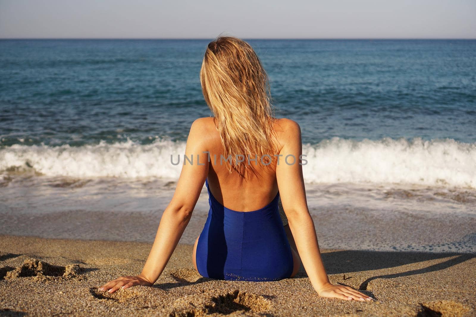 Young Woman Sunbathing At Tropical Beach. Woman in a blue swimsuit sits on the seashore on sand