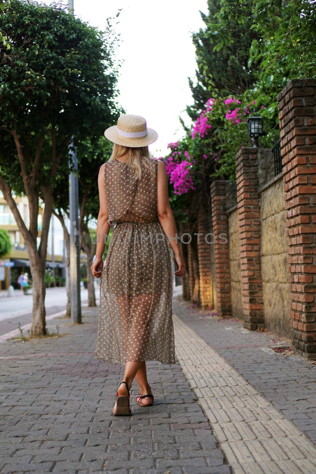 Young pretty girl walking on the summer turkey street. Vertical photo. A woman in a dress walks along a beautiful street with flowers. Alanya Turkey
