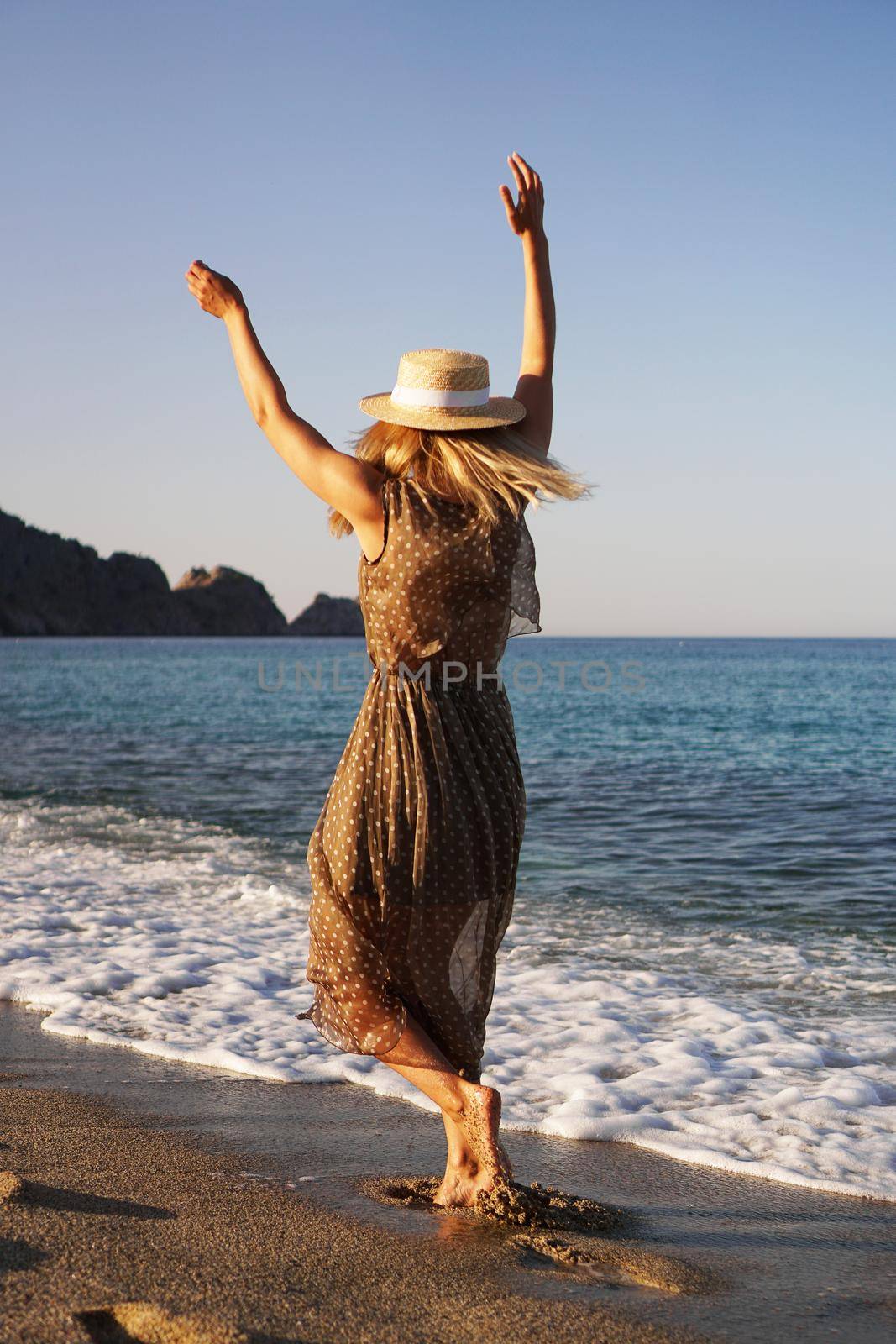 Woman on the beach in a brown dress and with a straw hat. Vacation on the beach of Turkey