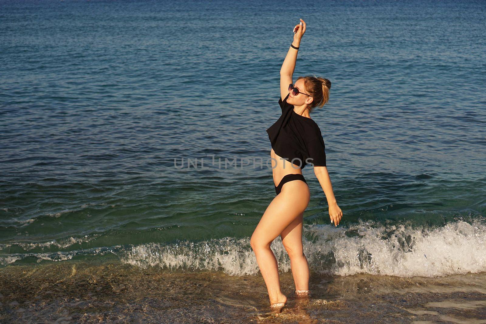 Young woman in a black tank top and underpants on the sea beach. Tanned body, body positive