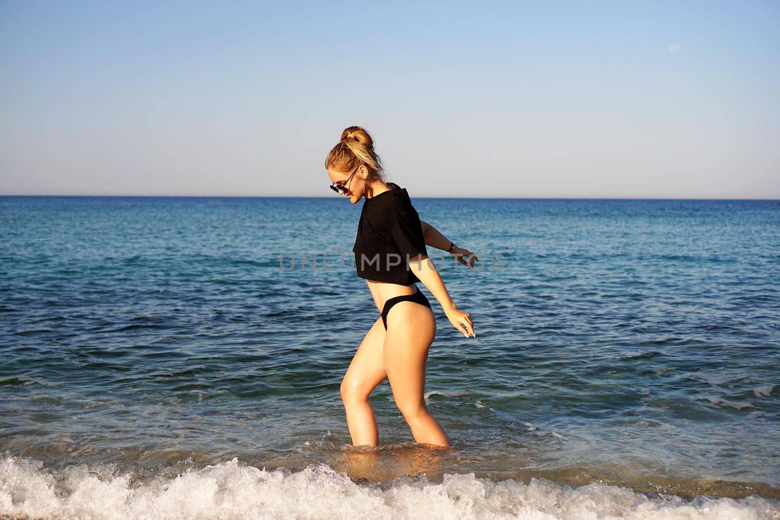 Young woman in a black tank top and underpants on the sea beach. Tanned body, body positive