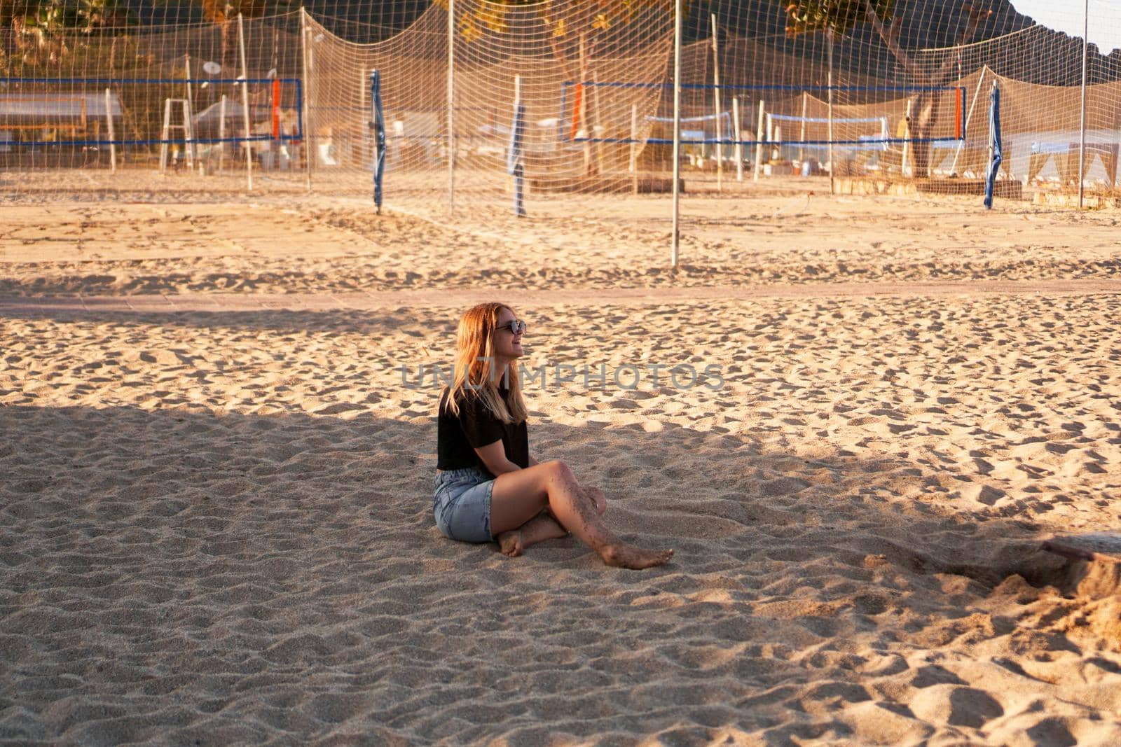 Woman at the summer beach in a hot day. Nearby there are palm trees and a sports volleyball court.
