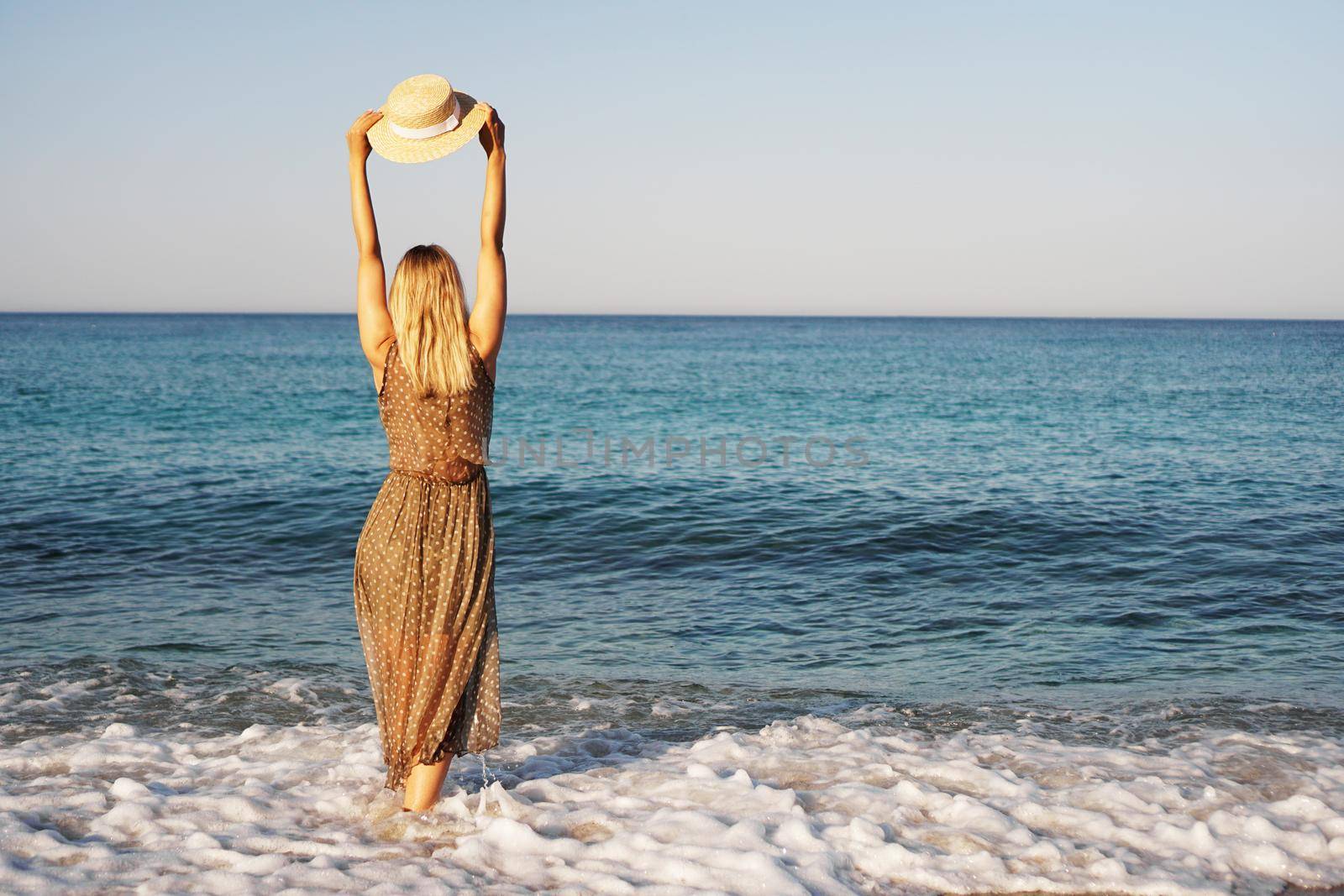 Woman on the beach in a brown dress and with a straw hat. Vacation on the beach of Turkey