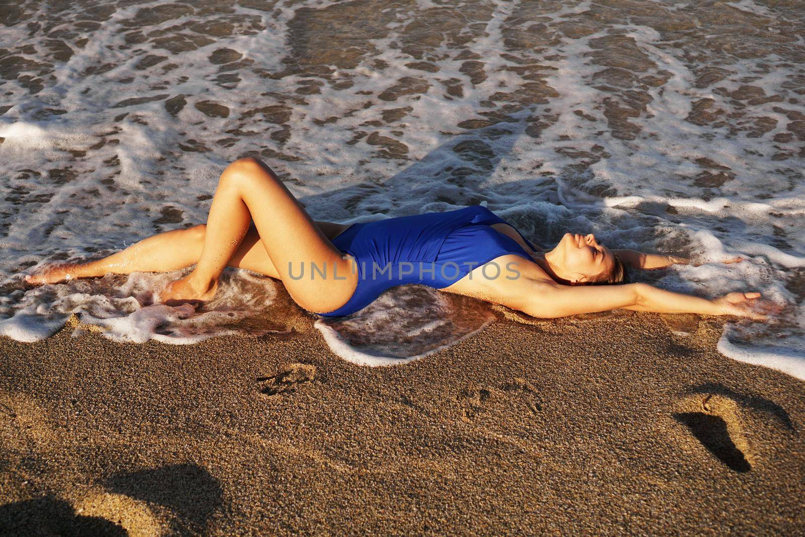 Young Woman Sunbathing At Tropical Beach. Woman in a blue swimsuit lies on the seashore on sand