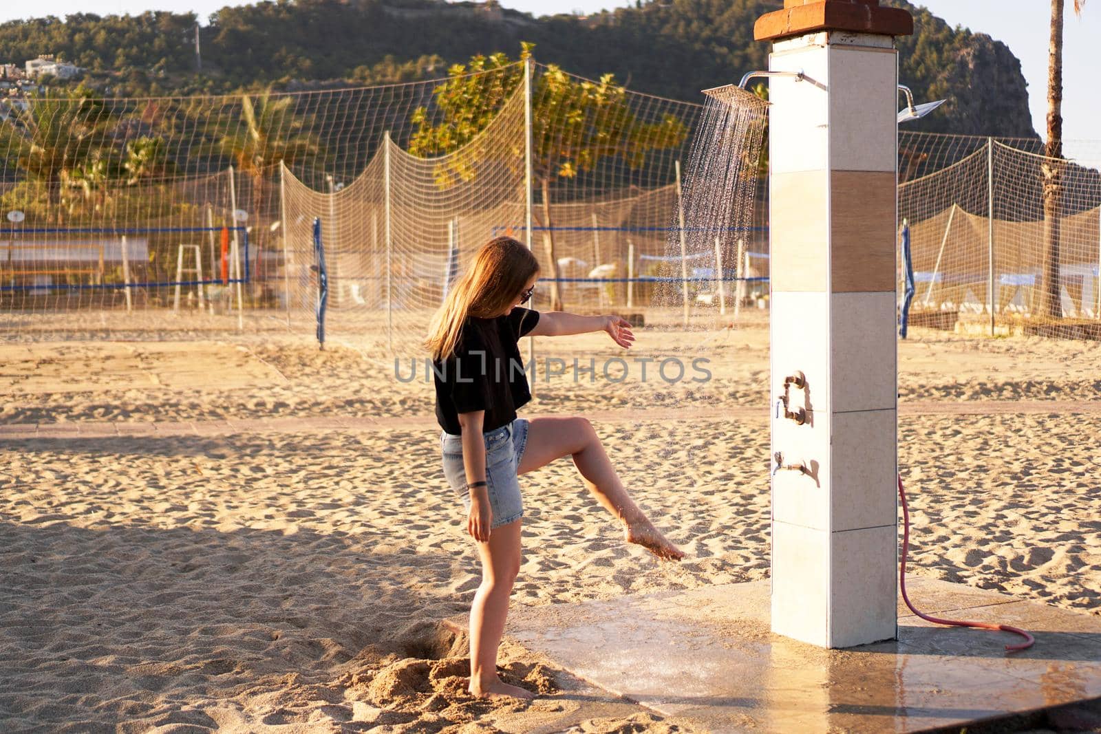 A girl in shorts and a black T-shirt on the beach near the shower. by natali_brill