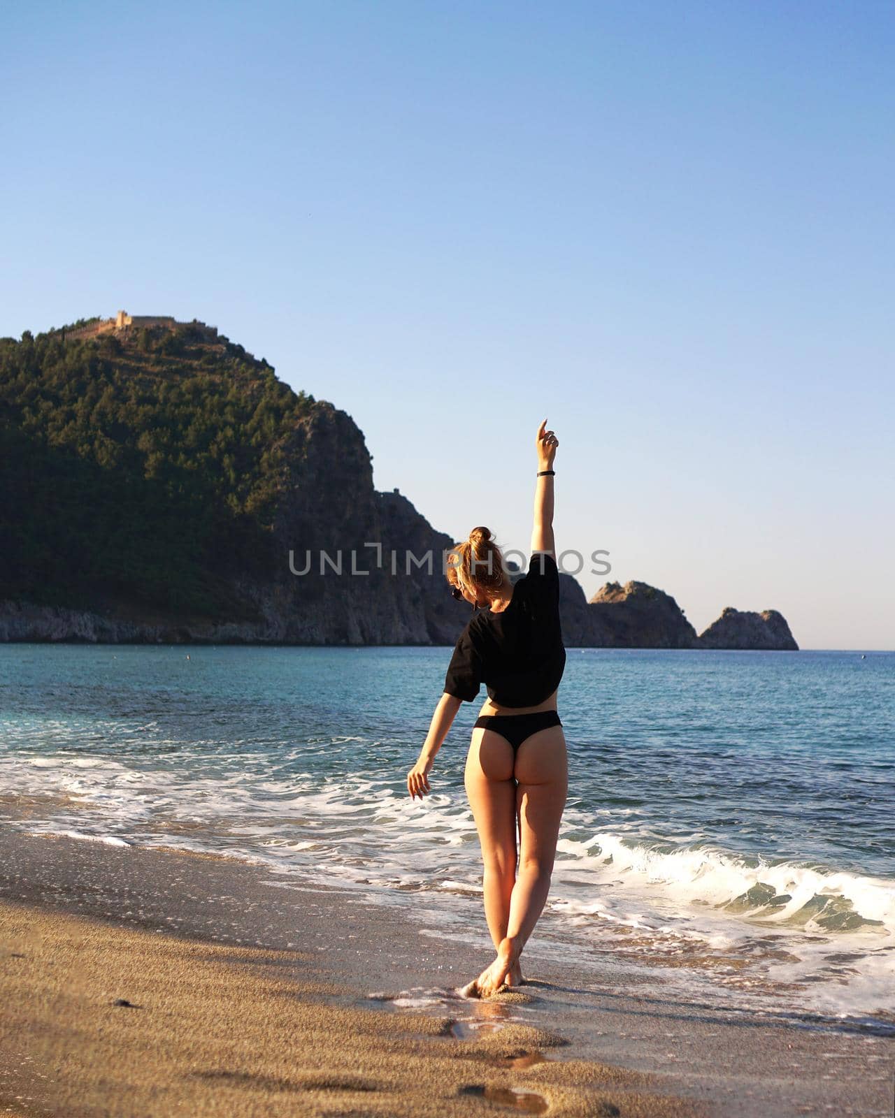 Young woman in a black tank top and underpants on the sea beach. Tanned body, body positive. Vertical photo