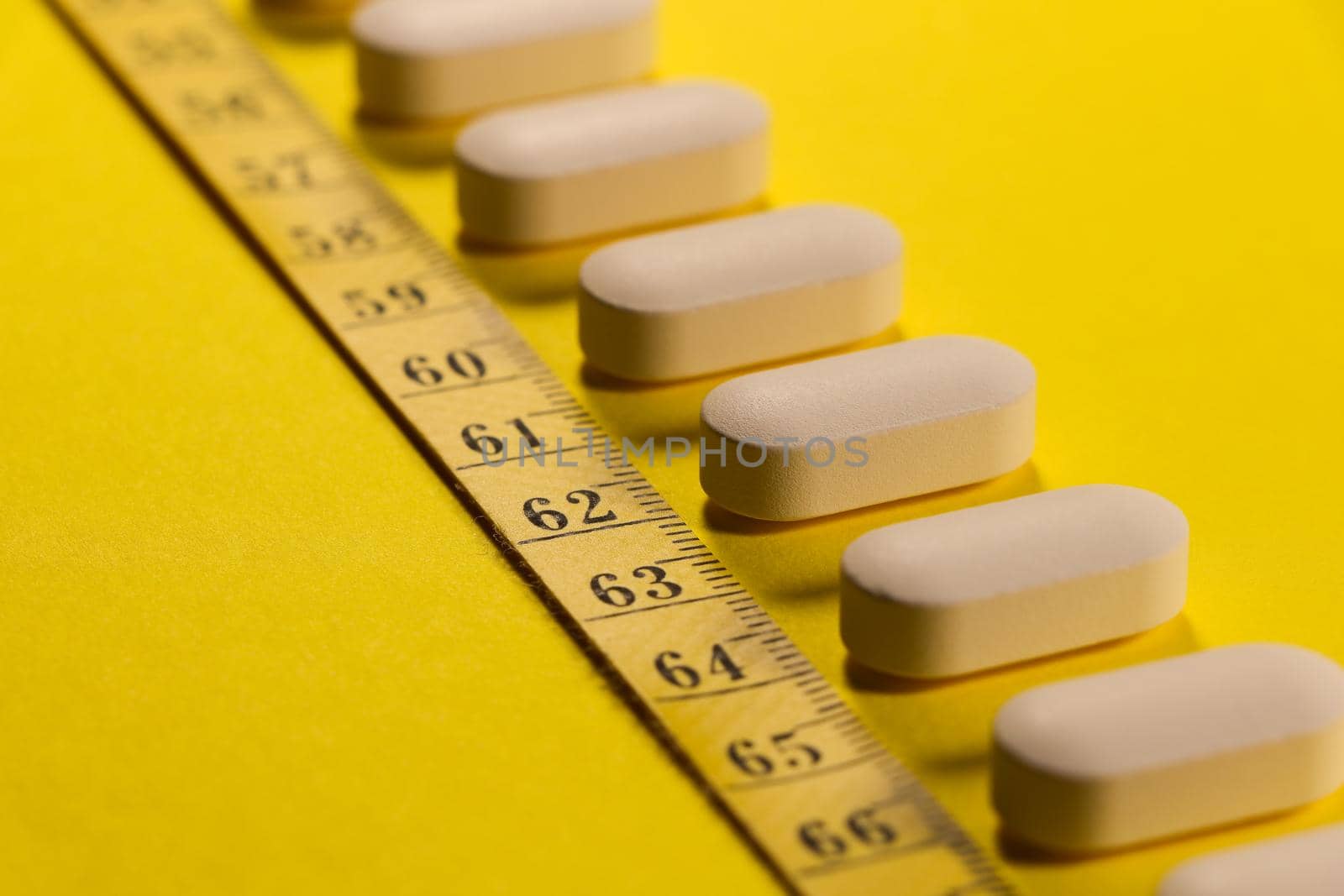 White tablet pills with measuring tape on bright yellow abstract weight-loss concept