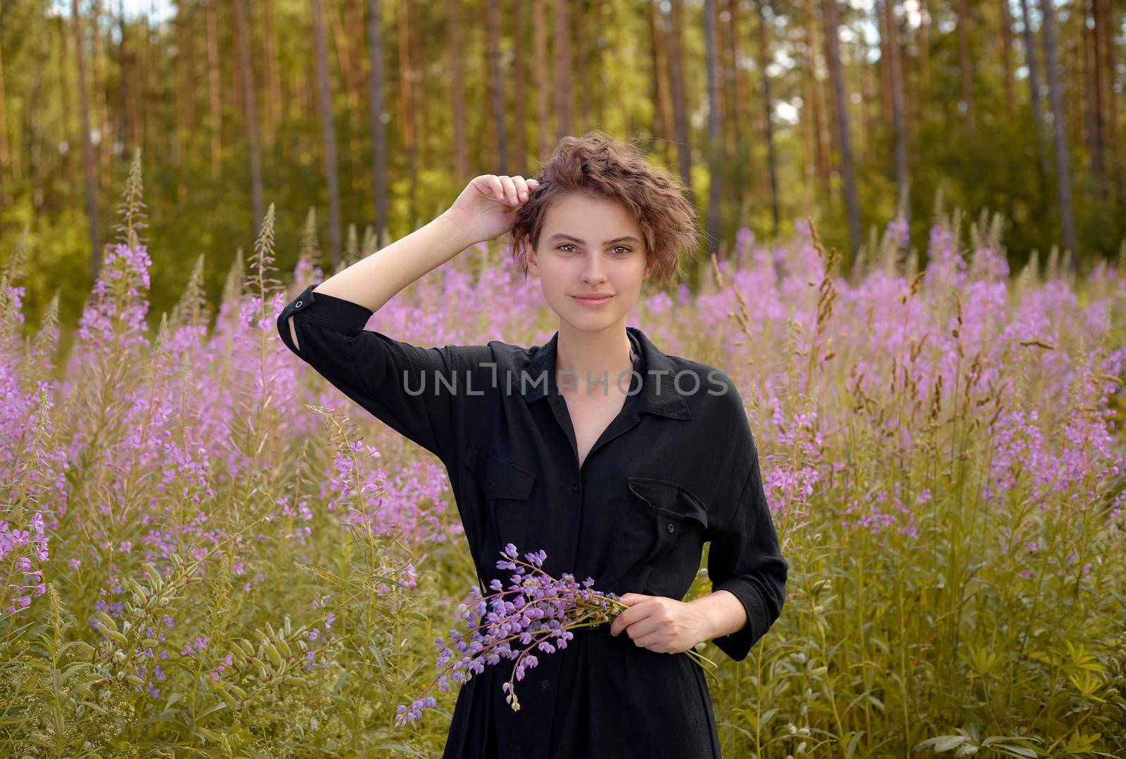 Young woman with a bouquet of lupines in her hand against the background of blooming Ivan-tea. Soft selective focus