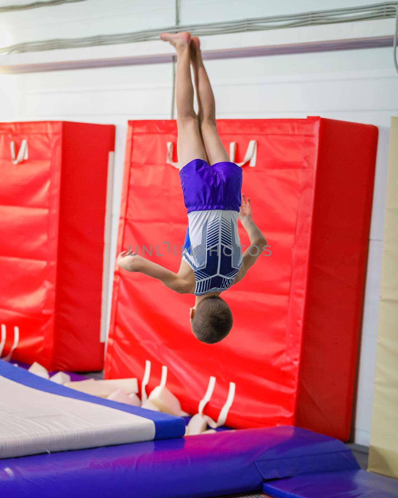 A young athlete performs a jump somersault in the gym. by Yurich32