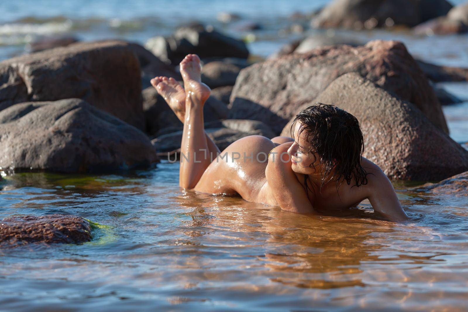 Nudity and a healthy lifestyle. Young nude woman with small breasts enjoys holiday at the seaside. Young nude woman lying in water on beach