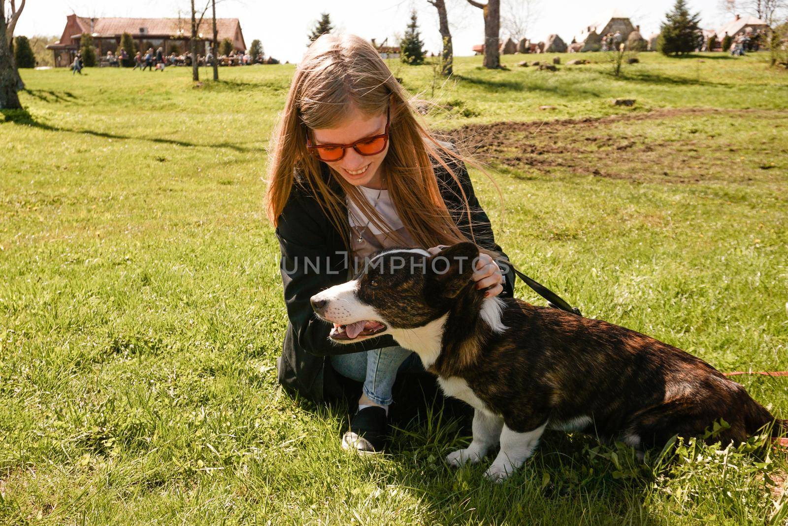 Young woman in red sunglasses plays with her corgi on a summer green lawn. Sunny day. Happy pet and owner