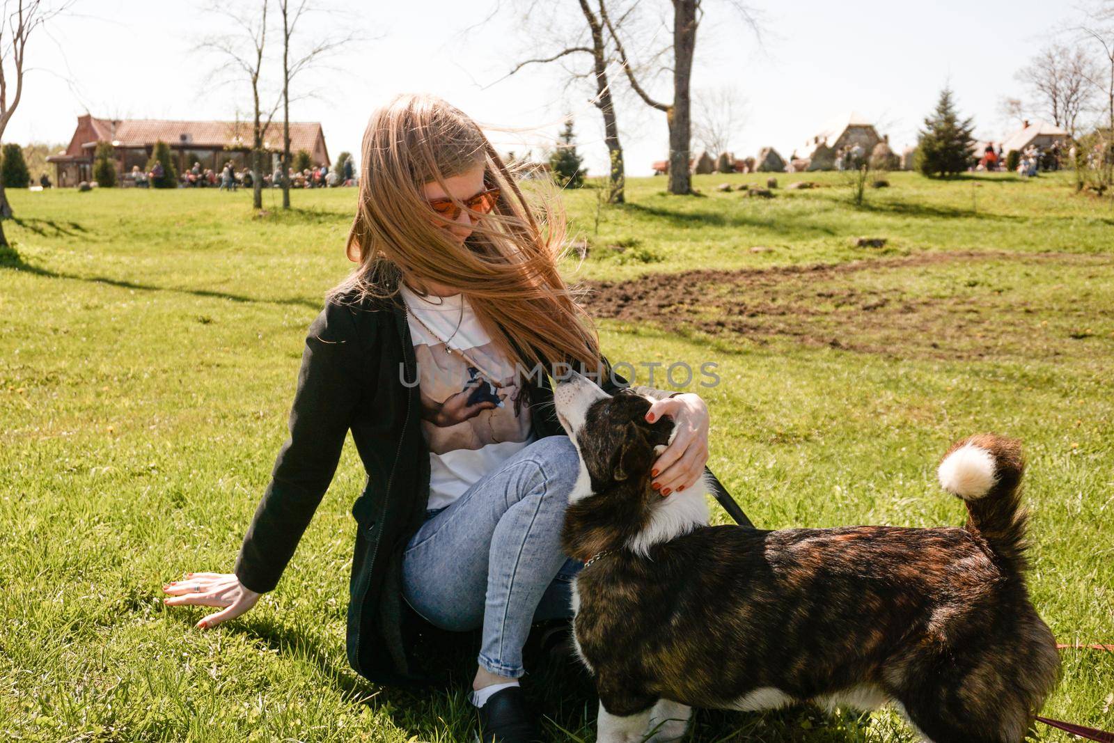 Young woman in red sunglasses plays with her corgi on a summer green lawn. Sunny day. Happy pet and owner