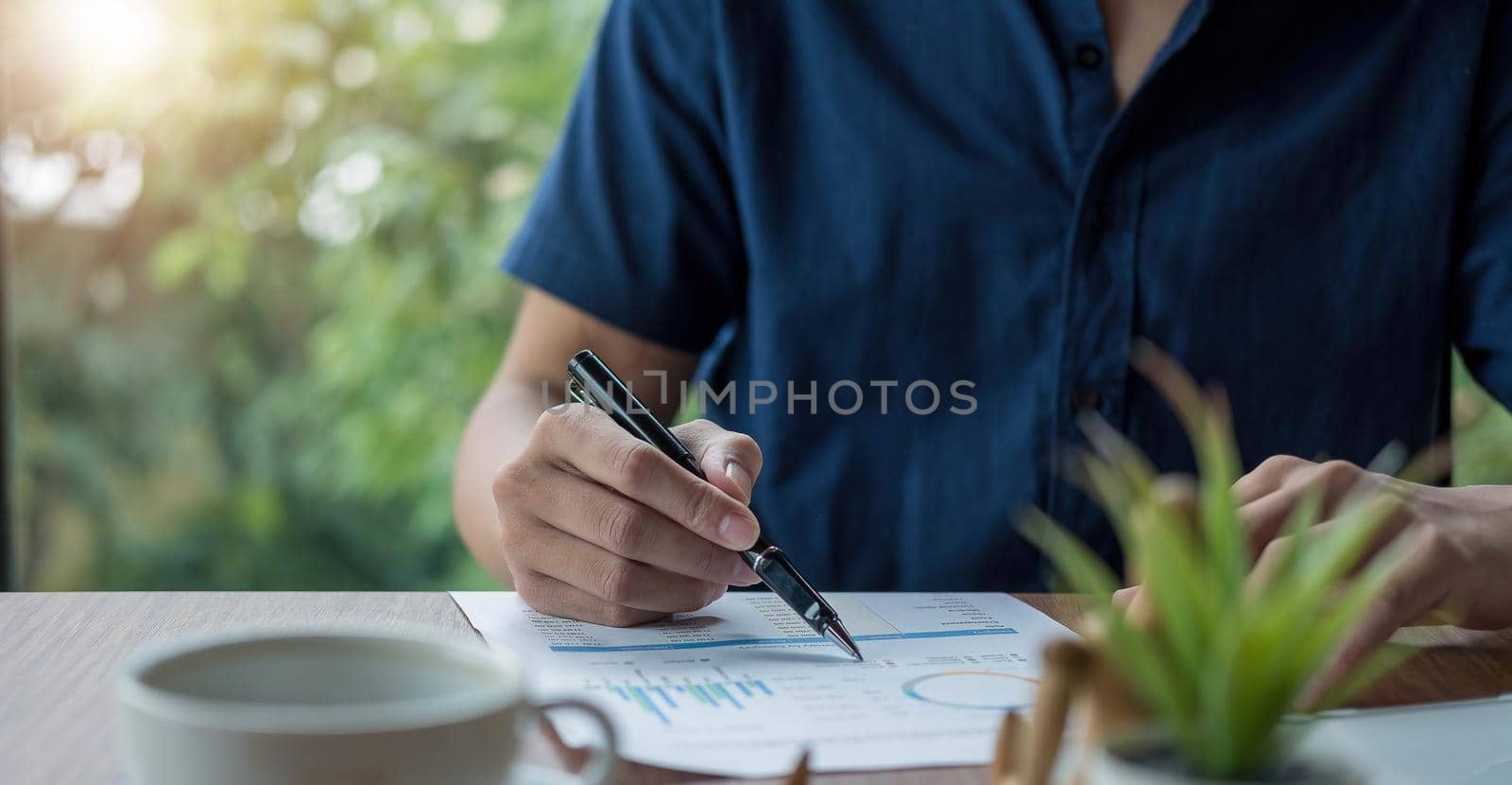 Businessman holding pen and pointing paper chart summary analyzing annual business report with using laptop at room office desk. by wichayada