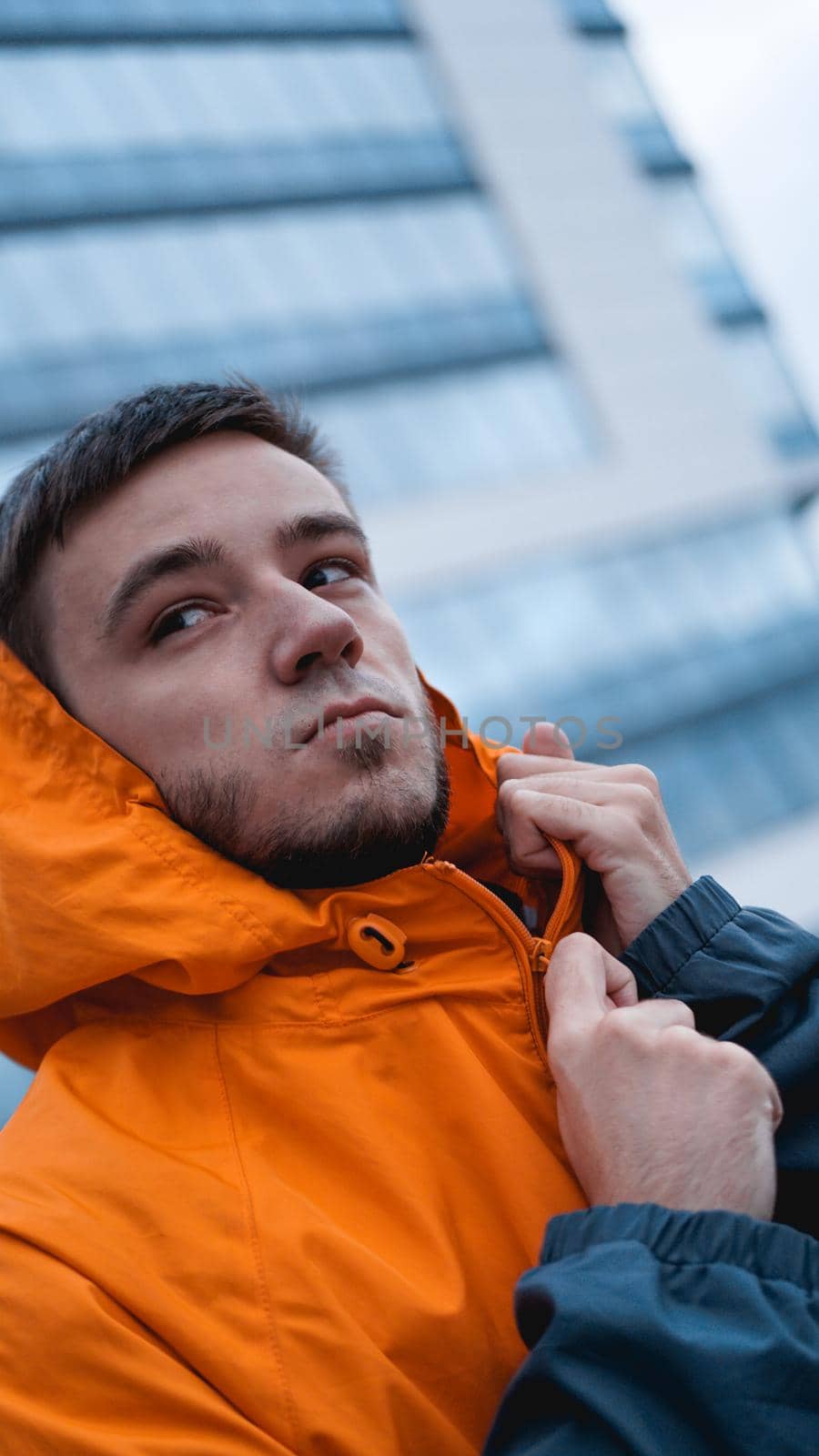 Young man in orange work uniform - blue glass building on background