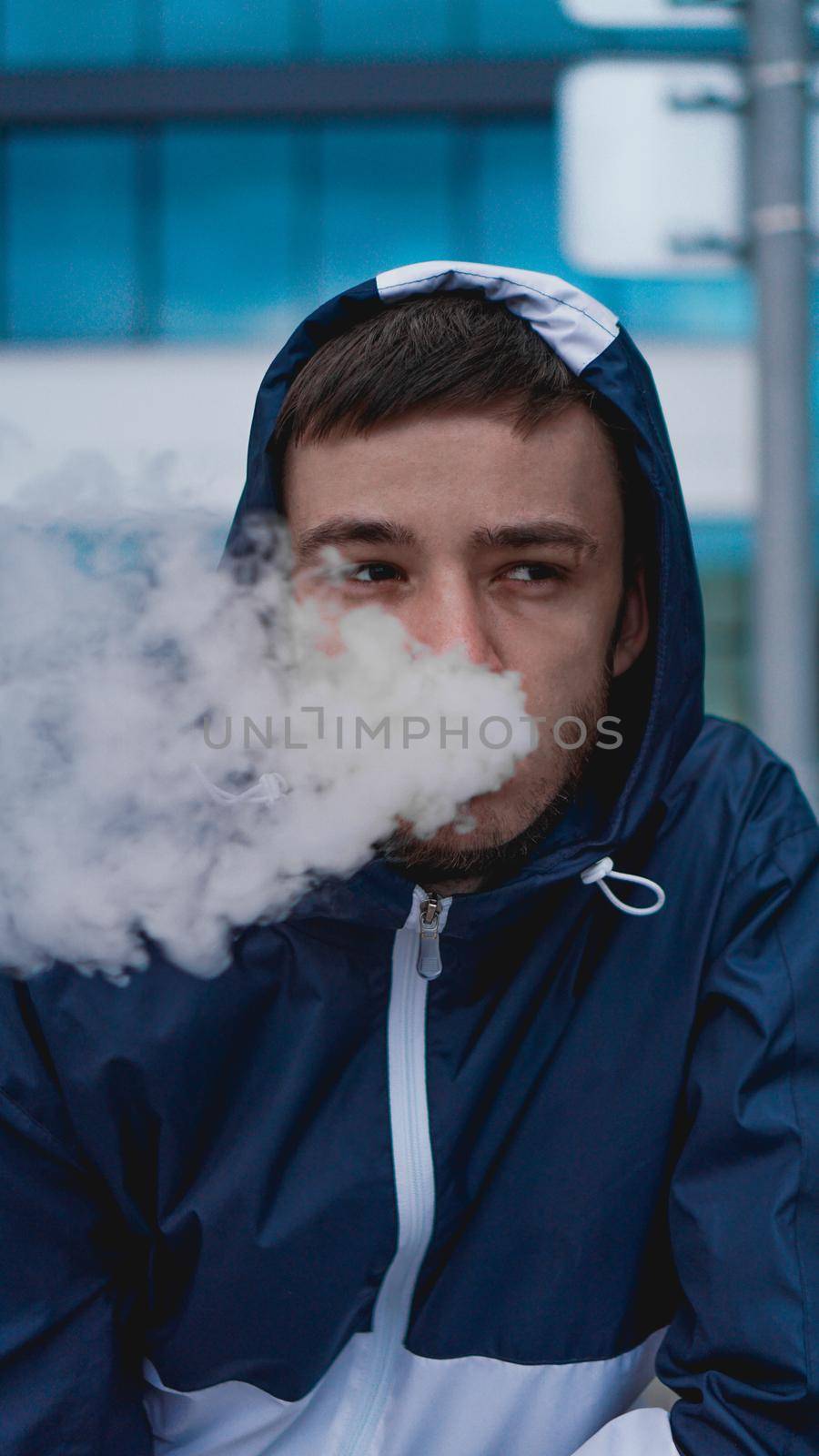 Man smoking electronic cigarette vapor. Smoking Electronic Cigarette against the background of a glass building