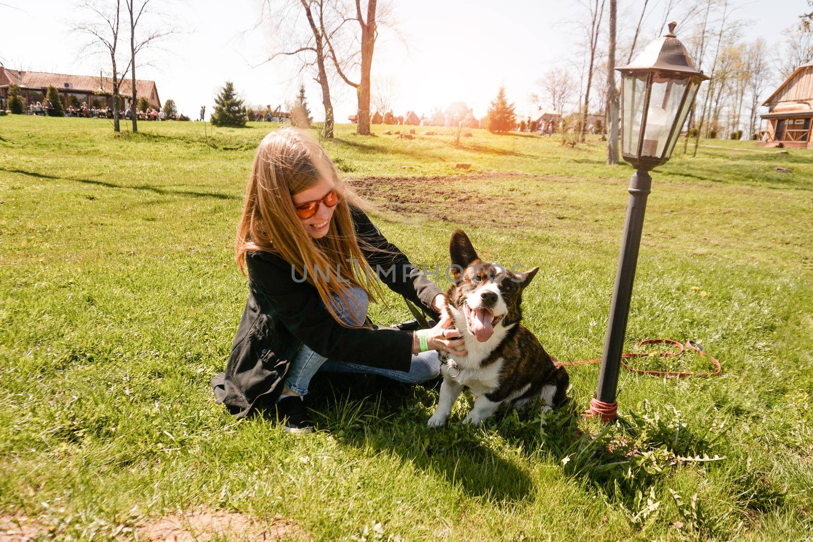 Young woman in red sunglasses plays with her corgi on a summer green lawn by natali_brill