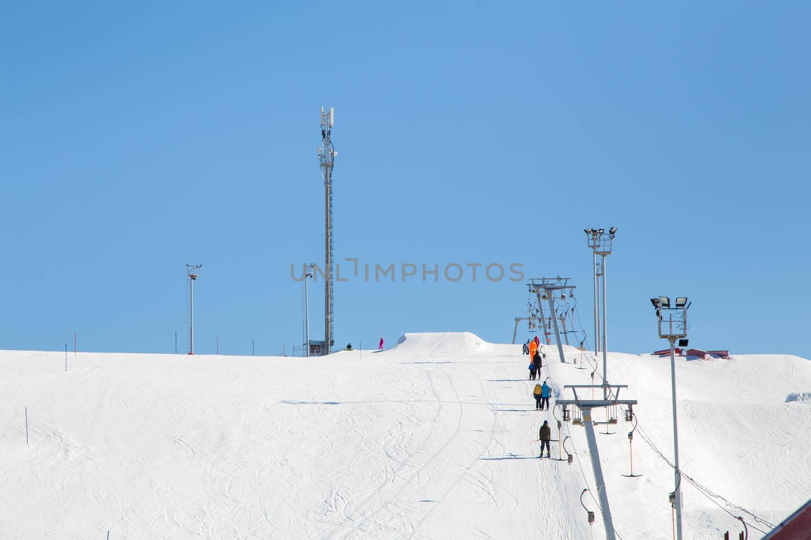 Ski resort, gentle snow slope with people on the lift going to the top. Mountain slope for skiing and snowboarding. Against the background of the blue sky. The summit and ski tours on a sunny day.