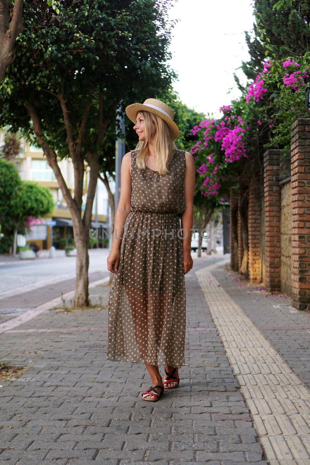 Vertical photo. A woman in a dress walks along a beautiful street with flowers by natali_brill