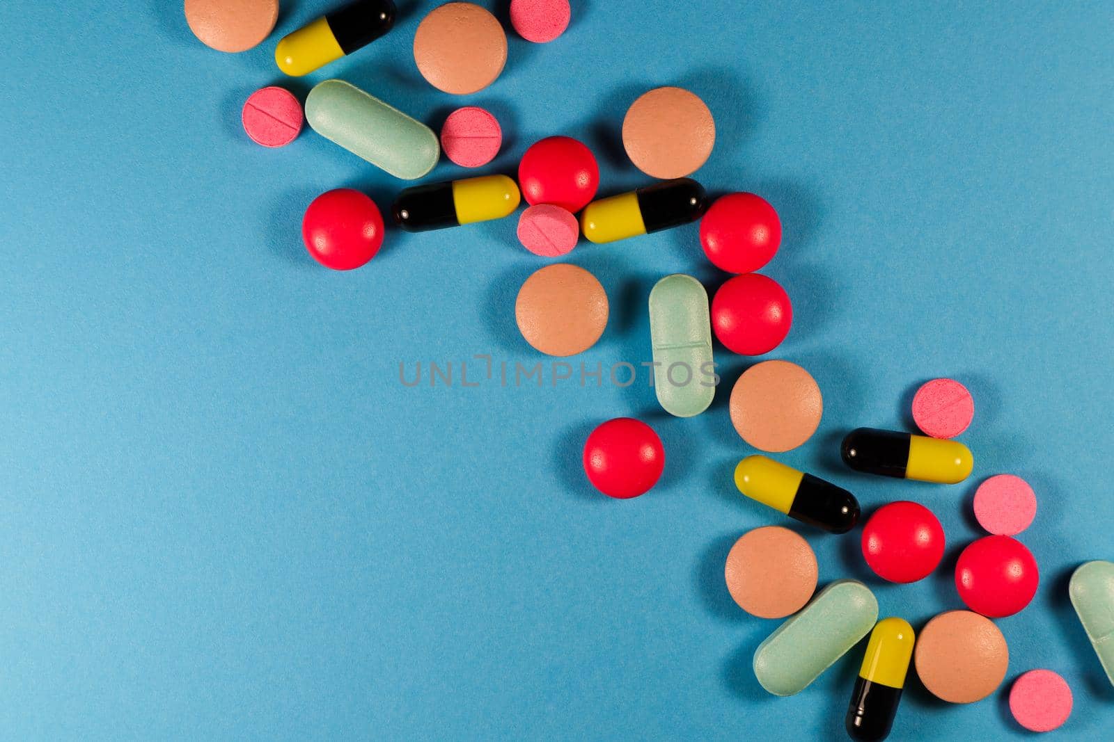 Variety of mixed pills and capsules in a diagonal line flat-lay abstract on blue background